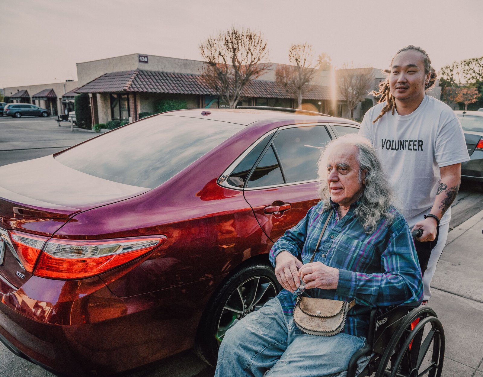 Caregiver assisting an older man using a wheelchair near a vehicle