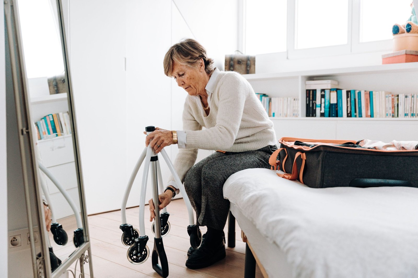 Older woman packing a suitcase with a rollator beside her in a bedroom