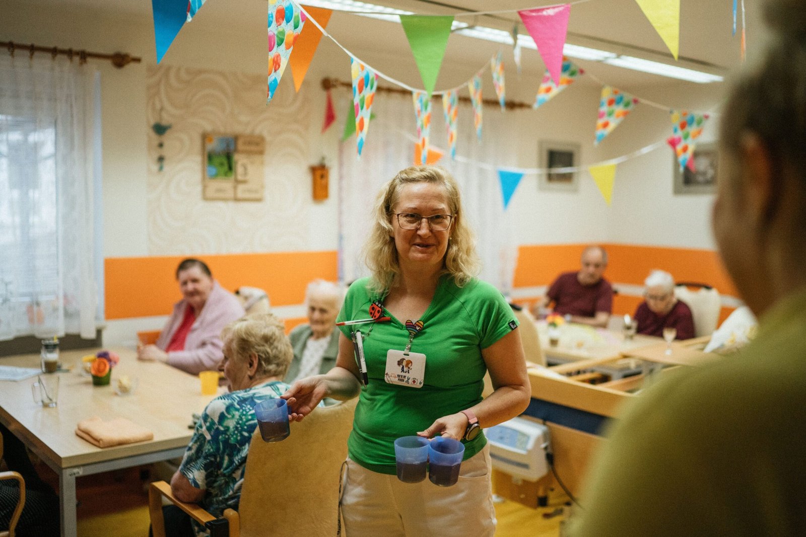 Caregiver serving drinks and assisting older residents in a nursing home dining area