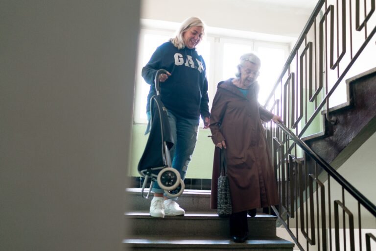 Caregiver assisting an older woman while she walks down indoor stairs