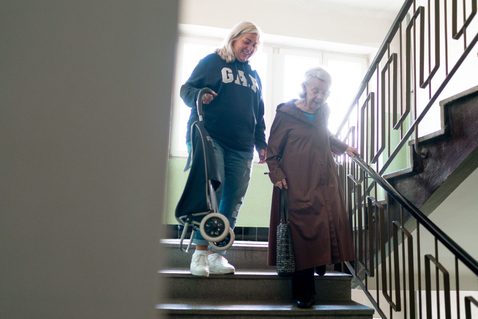 Caregiver assisting an older woman while she walks down indoor stairs