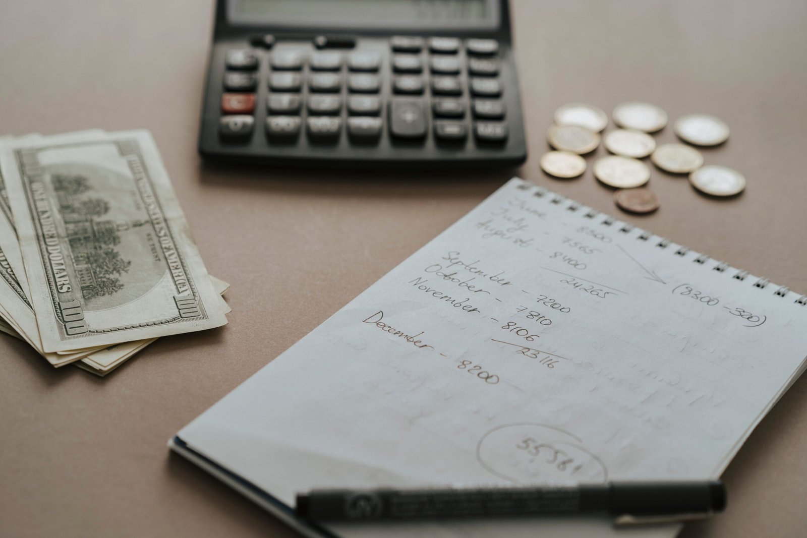 Budget notebook, calculator, cash, and coins arranged on a desk.