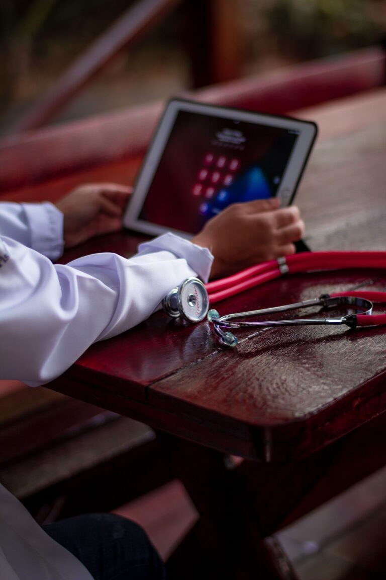 Hands using a tablet beside a red stethoscope on a wooden table.