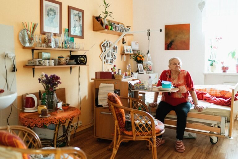 Older woman seated in a warmly furnished retirement-home room.