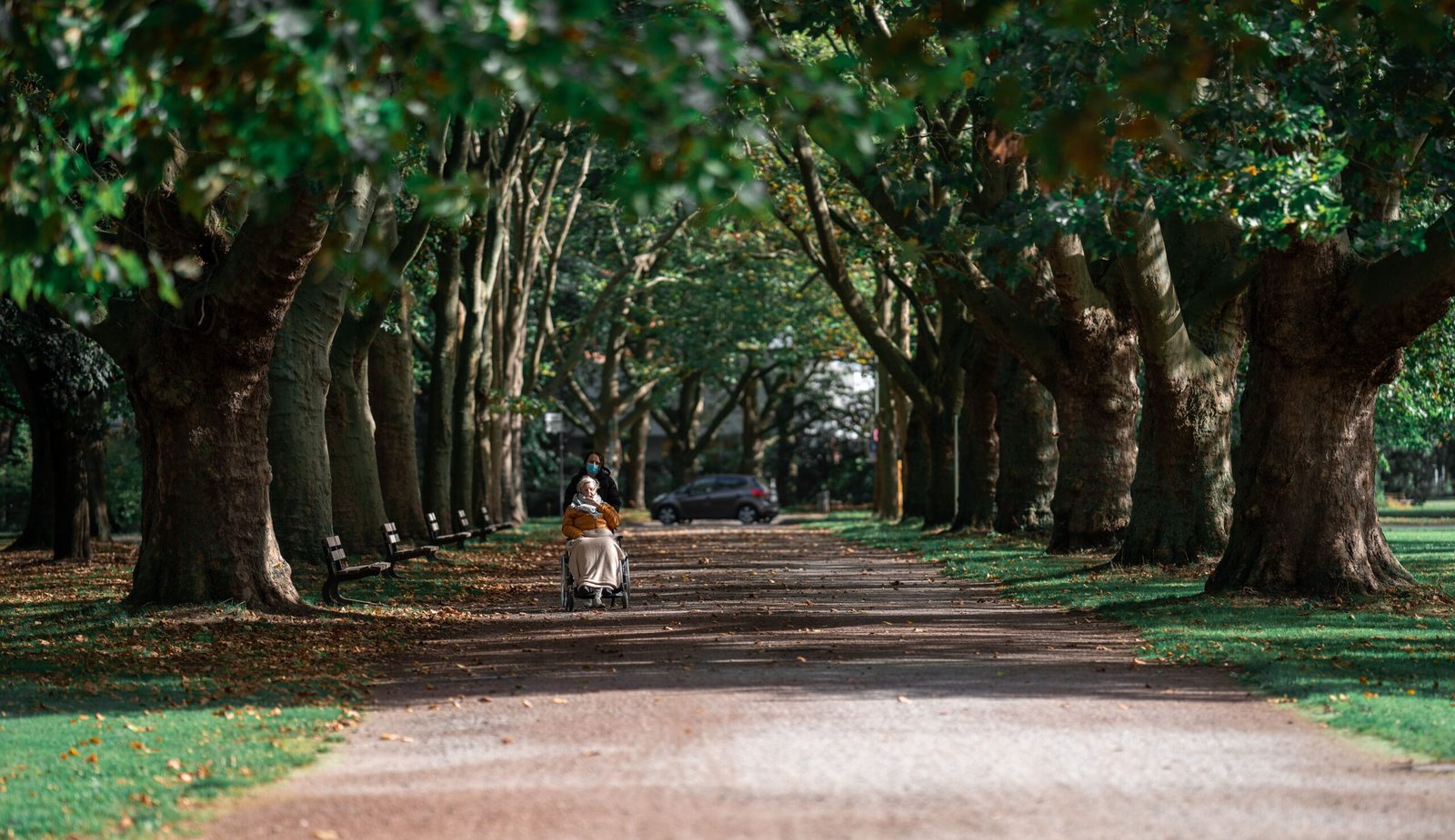 Caregiver accompanying an older woman in a wheelchair along a park path