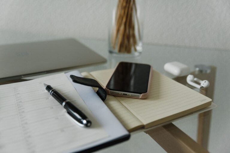 Smartphone and black pen resting on an open notebook on a desk.
