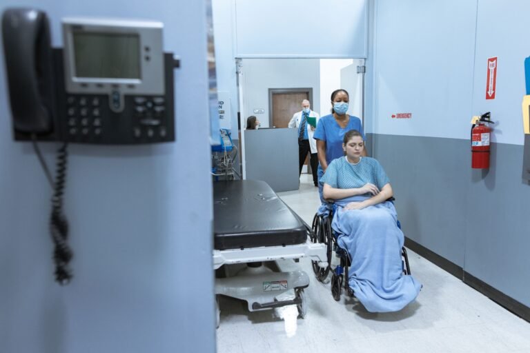Nurse assisting a wheelchair user through a healthcare corridor.