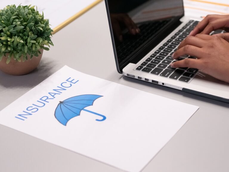 Hands typing on a laptop beside an insurance document.