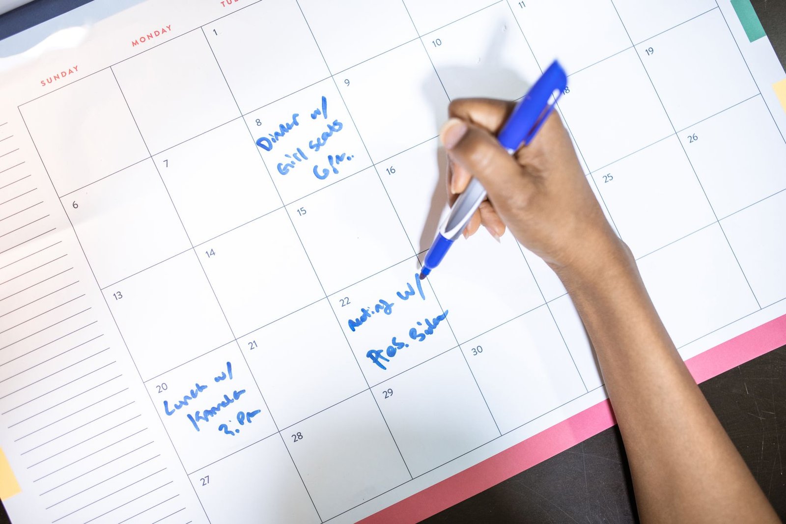 Hand writing an appointment on a paper calendar with a blue pen.