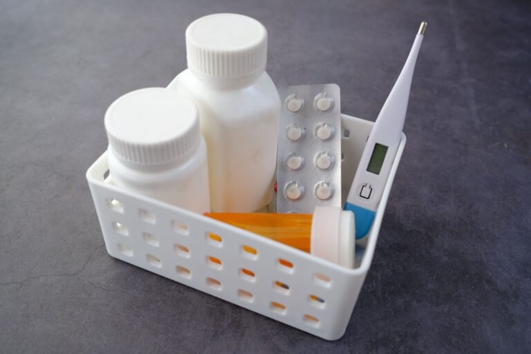 Medication bottles, blister packs, and a thermometer organized in a healthcare box.