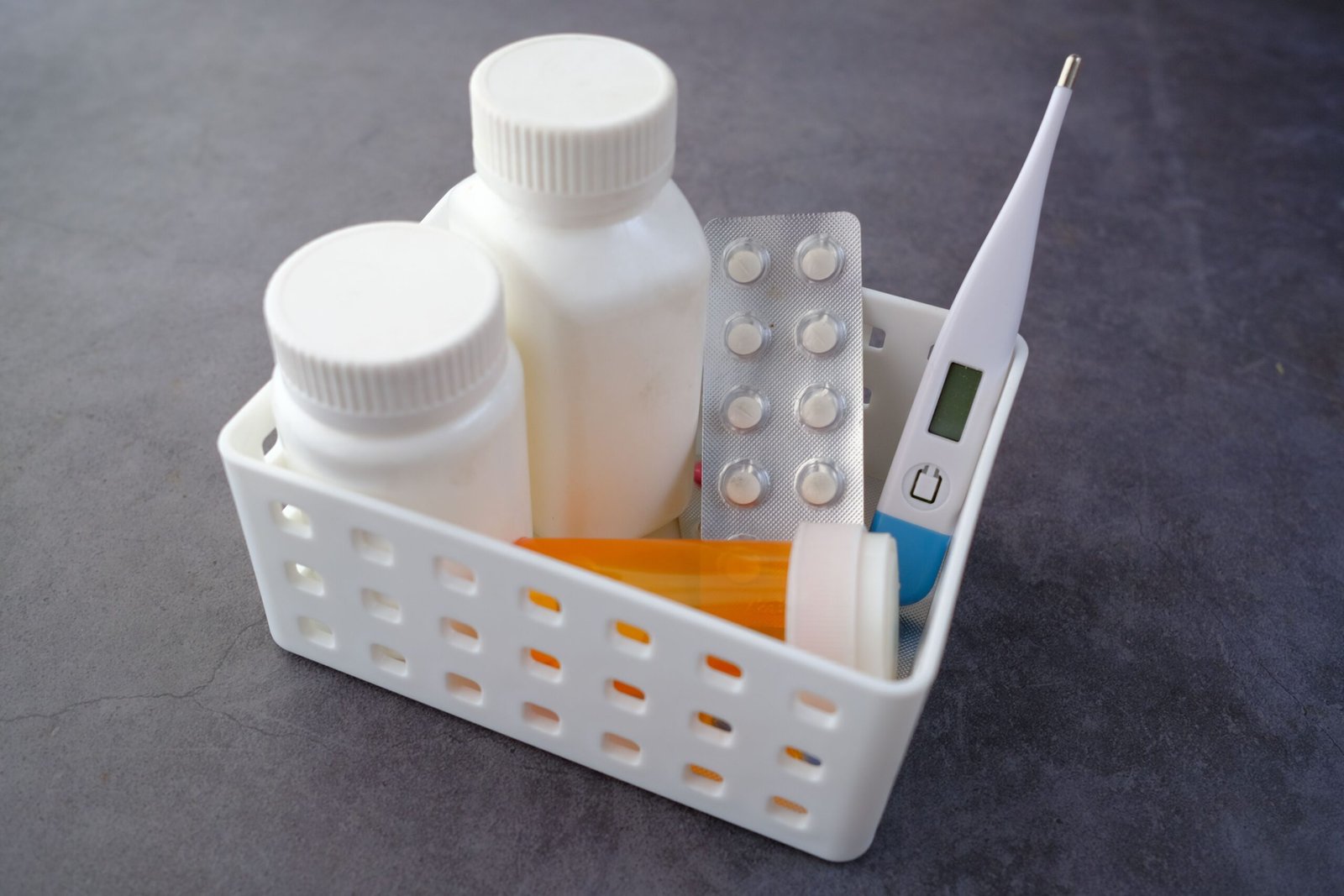 Medication bottles, blister packs, and a thermometer organized in a healthcare box.