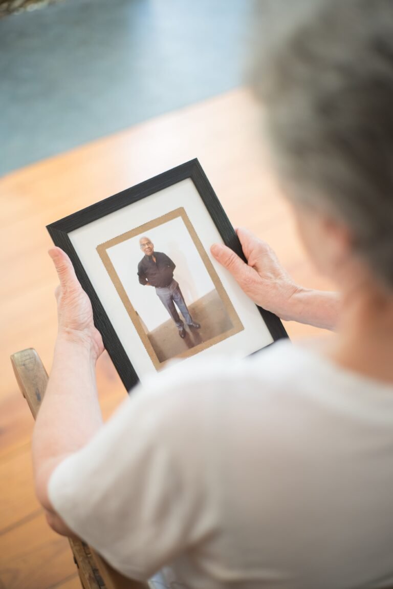 Older woman sitting indoors while looking thoughtfully at a framed photograph