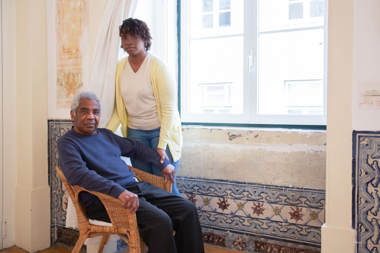 Older man seated beside a caregiver near a window