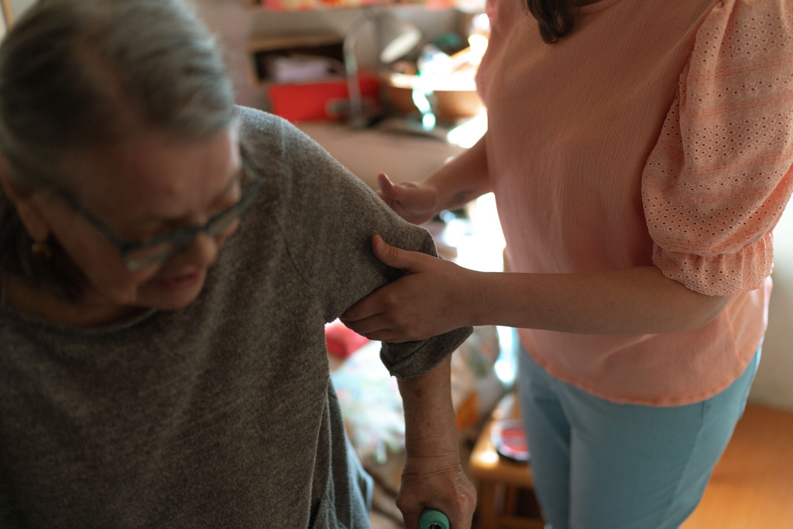 Caregiver supporting an older woman with mobility inside a home