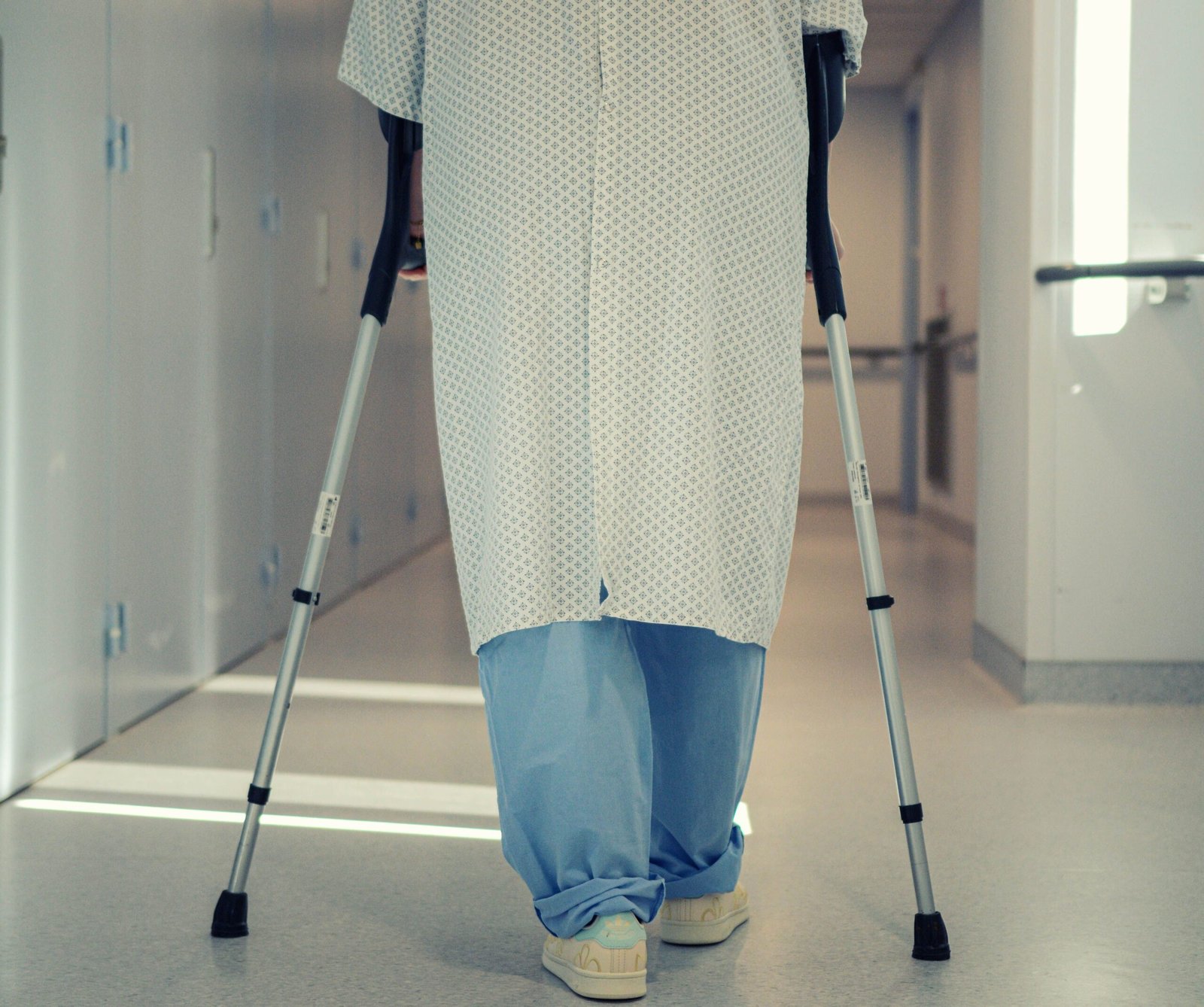 Older adult walking with crutches in a hospital corridor.