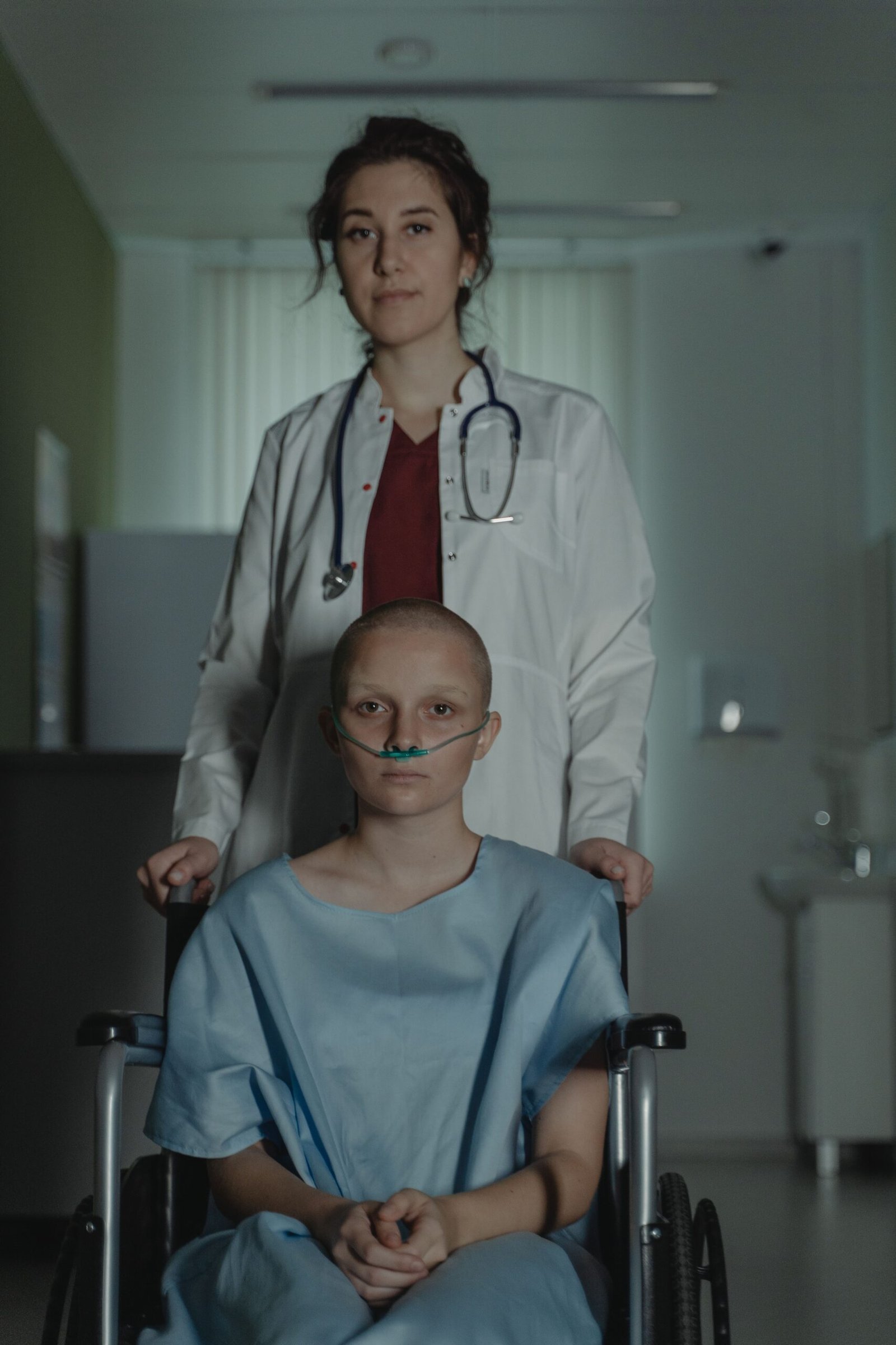 Healthcare professional assisting a wheelchair user in a hospital hallway.