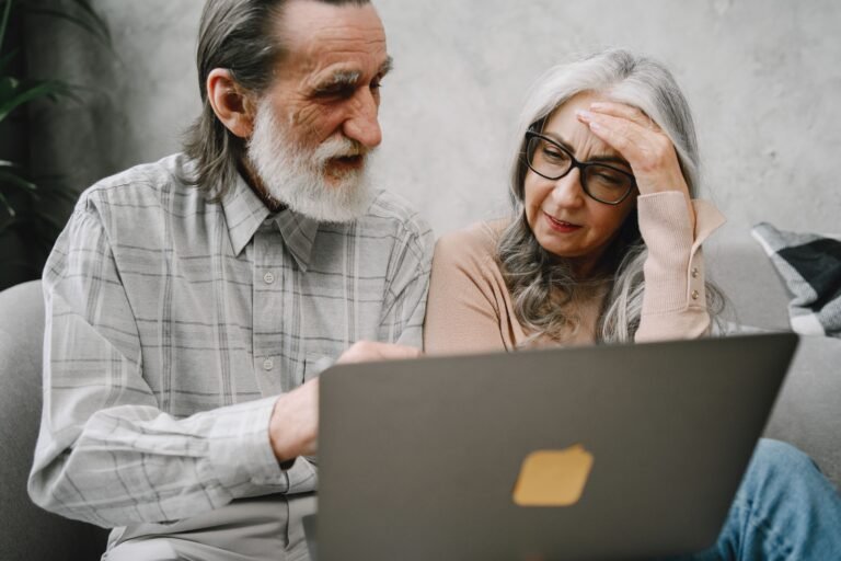 Older couple using a laptop together during a calm home conversation.